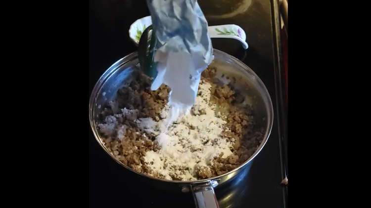 Adding flour to sausage gravy.